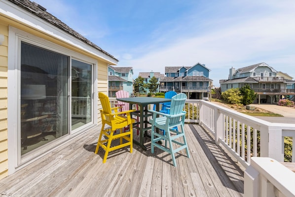 A wooden deck with a table and chairs, overlooking a row of houses.