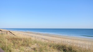 Ein Strand mit einer Holzpromenade und grasbewachsenen Dünen.