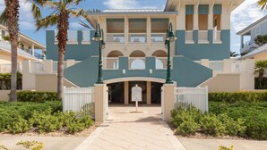 A two-story building with a central entrance, surrounded by palm trees and a white picket fence. - Cinnamon Beach 741 - Direct Oceanfront Corner Unit! New Living Room! (Palm Coast)