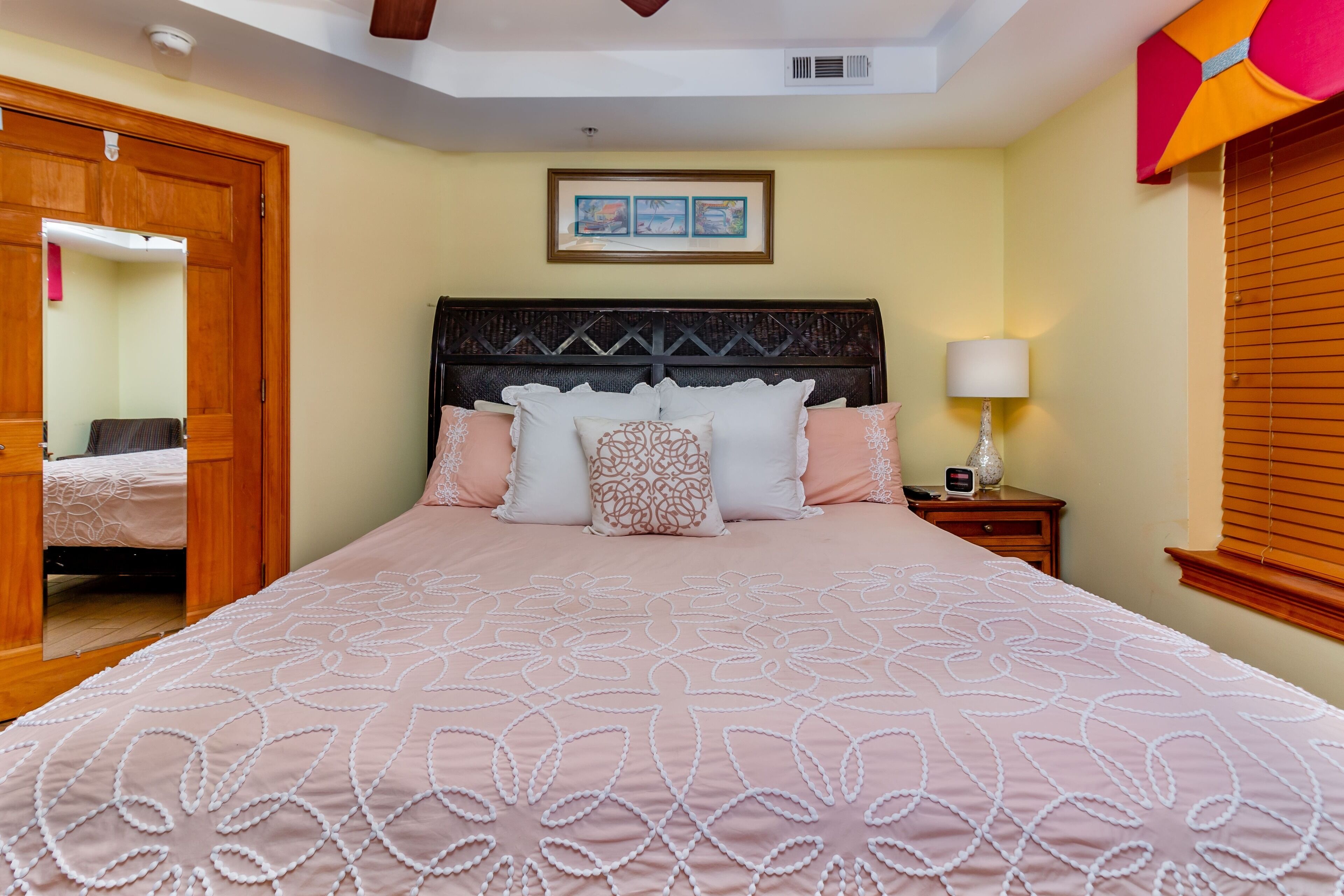 A neatly made bed with a patterned bedspread, a wooden headboard, and a bedside lamp.