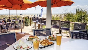 An outdoor dining area with tables and chairs, umbrellas, and a view of the beach. - Late Summer Savings • Beachside Colony • Tybee’s ONLY Oceanfront Resort• 2BR/2BA (Tybee Island)