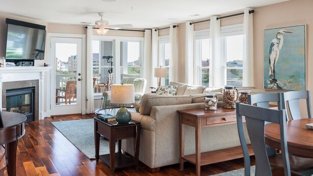 A spacious living room with a fireplace, a sofa, a dining table, and a painting on the wall. - Sound, Mind and Bodie: Condo, Shared Pool (Manteo)