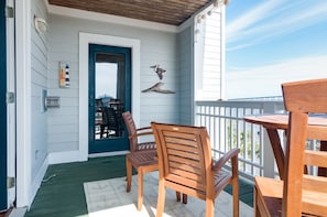 A covered porch with wooden chairs and a table, a door with a blue frame, and decorative wall art.