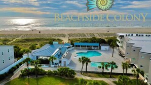 Un complexe hôtelier doté d’une piscine, offrant une vue sur la plage et arborant le logo de Beachside Colony.