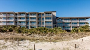 Un hotel frente a la playa con varios balcones y una playa arenosa al frente.