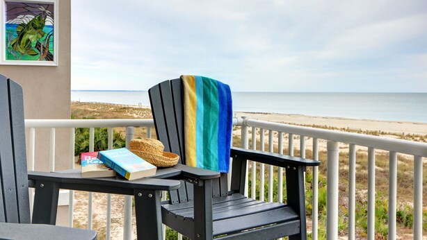 Una silla con una toalla a rayas, un libro y una cesta en un balcón con vistas a la playa.