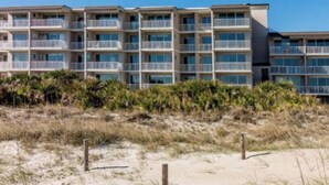 A beachfront hotel with multiple balconies, a sandy beach in front, and a clear sky. - Summer & July 4th Savings at Beachside Colony Tybee's ONLY Oceanfront Resort 3/2 (Tybee Island)