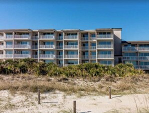 A beachfront hotel with multiple balconies, a sandy beach in front, and a clear sky.
