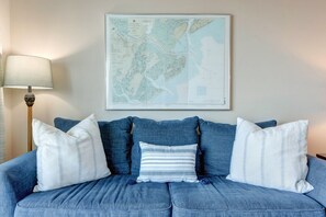 A blue sofa with white and striped pillows, a map on the wall, and a lamp on the left.