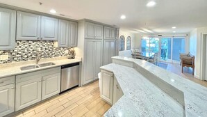 A modern kitchen with grey cabinets, a tiled backsplash, and a large island. - Late Summer Savings • Beachside Colony • Tybee’s ONLY Oceanfront Resort• 3BR/2BA (Tybee Island)