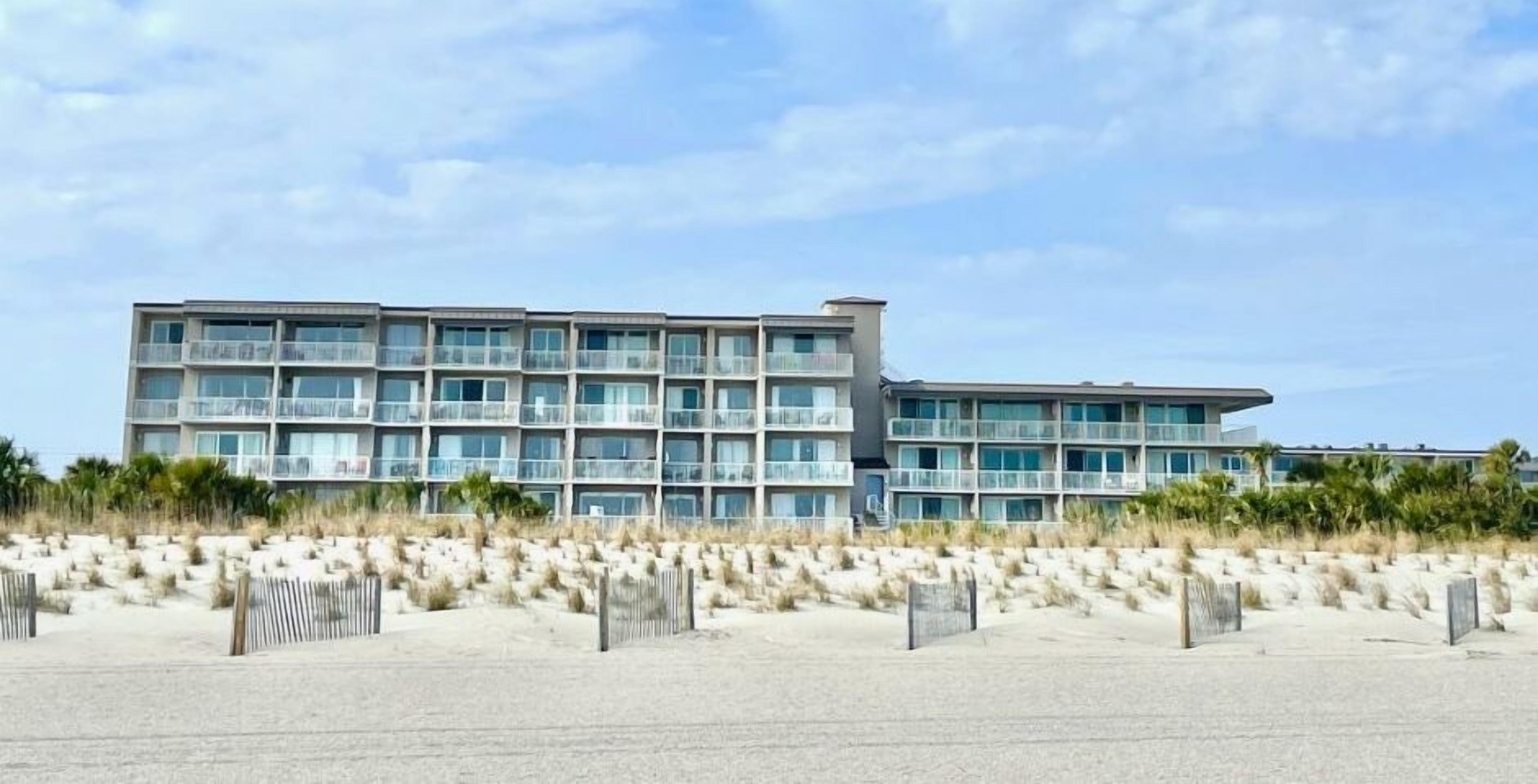 A modern multi-story hotel with balconies, located near a sandy beach.