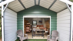 Un petit abri de jardin vert, avec un toit en métal, une table, deux chaises et un banc à l’intérieur.