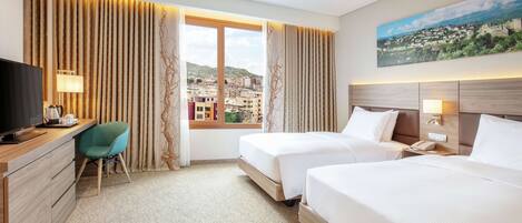 A hotel room with two beds, a desk, a chair, and a large window with a city view.