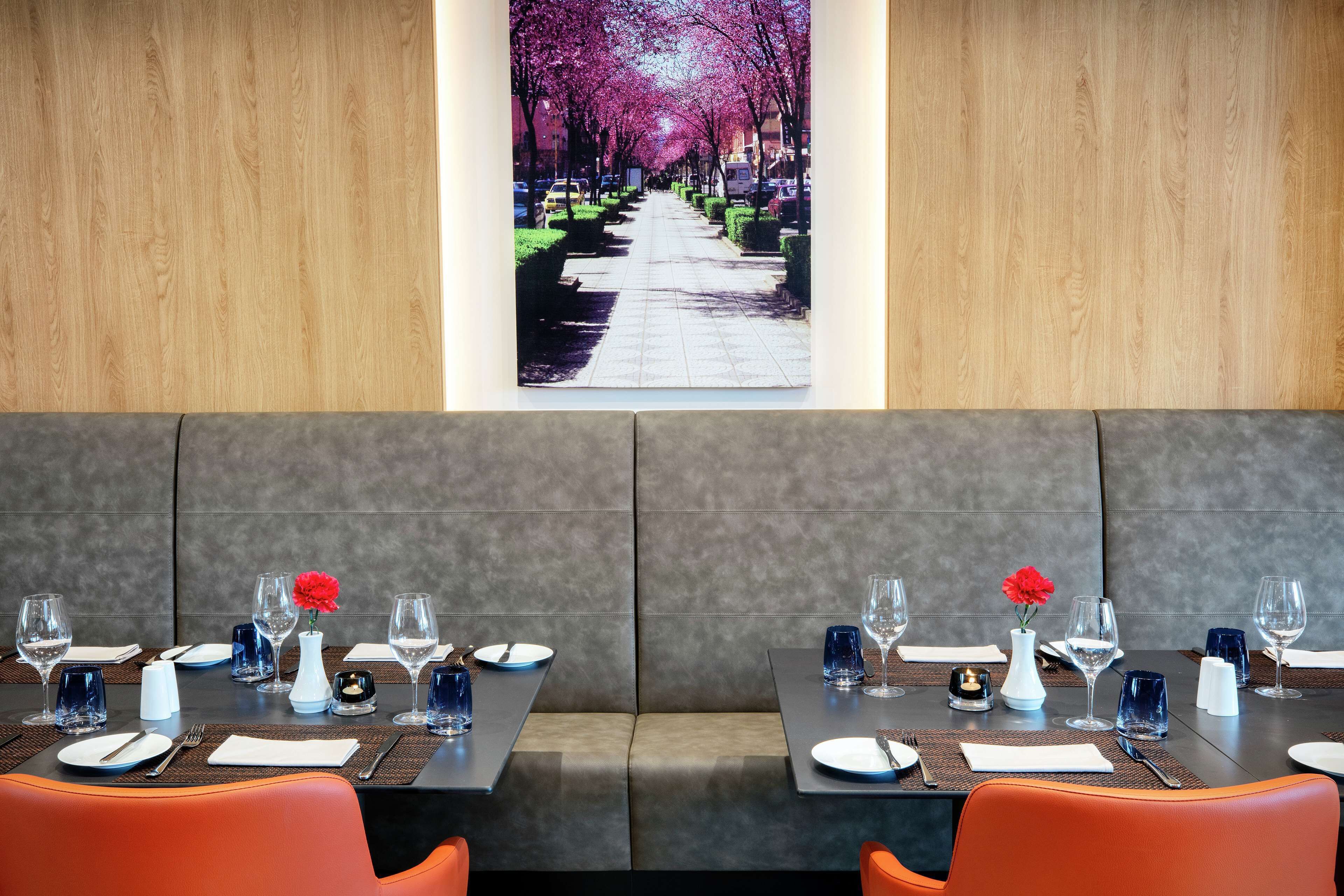 A restaurant with a view of a tree-lined street. Tables are set with plates, glasses, and cutlery.