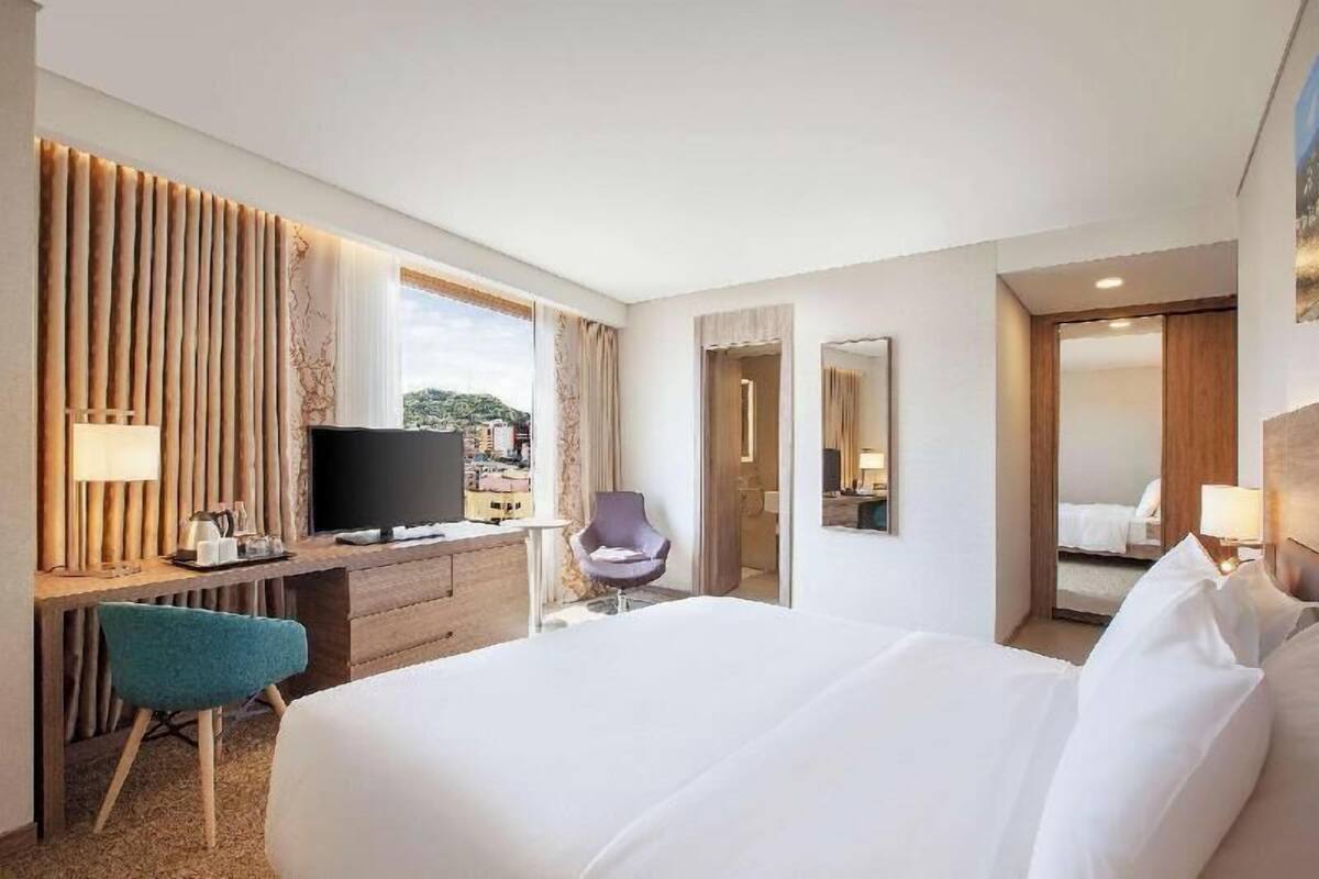 A hotel room with a bed, a desk with a TV, a chair, and a mirror.