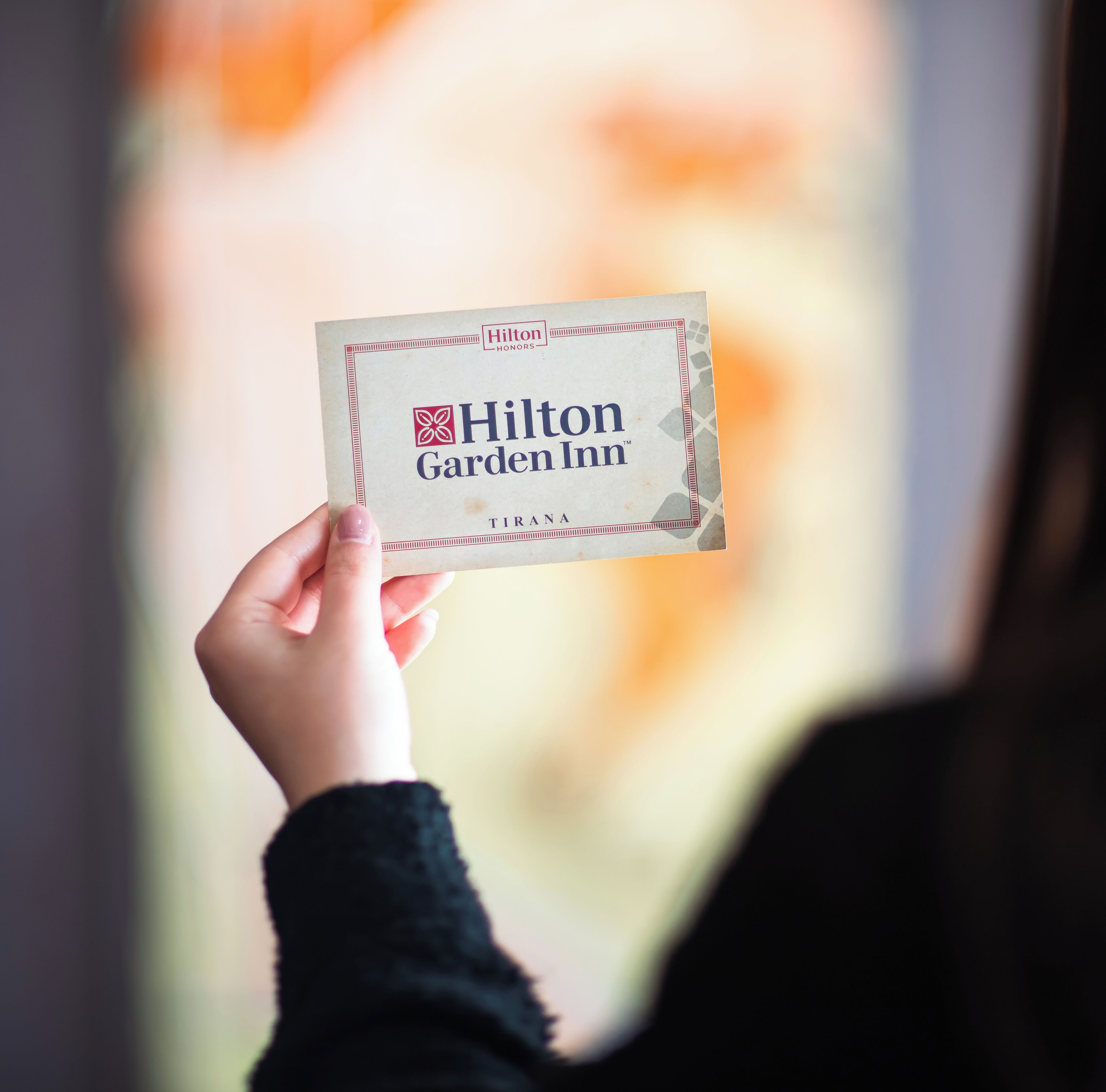 Une main tenant une carte de visite du Hilton Garden Inn de Tirana.