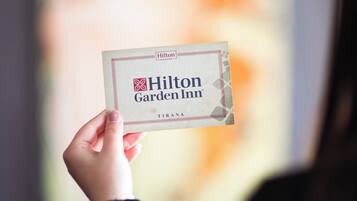 Une main tenant une carte de visite du Hilton Garden Inn de Tirana.