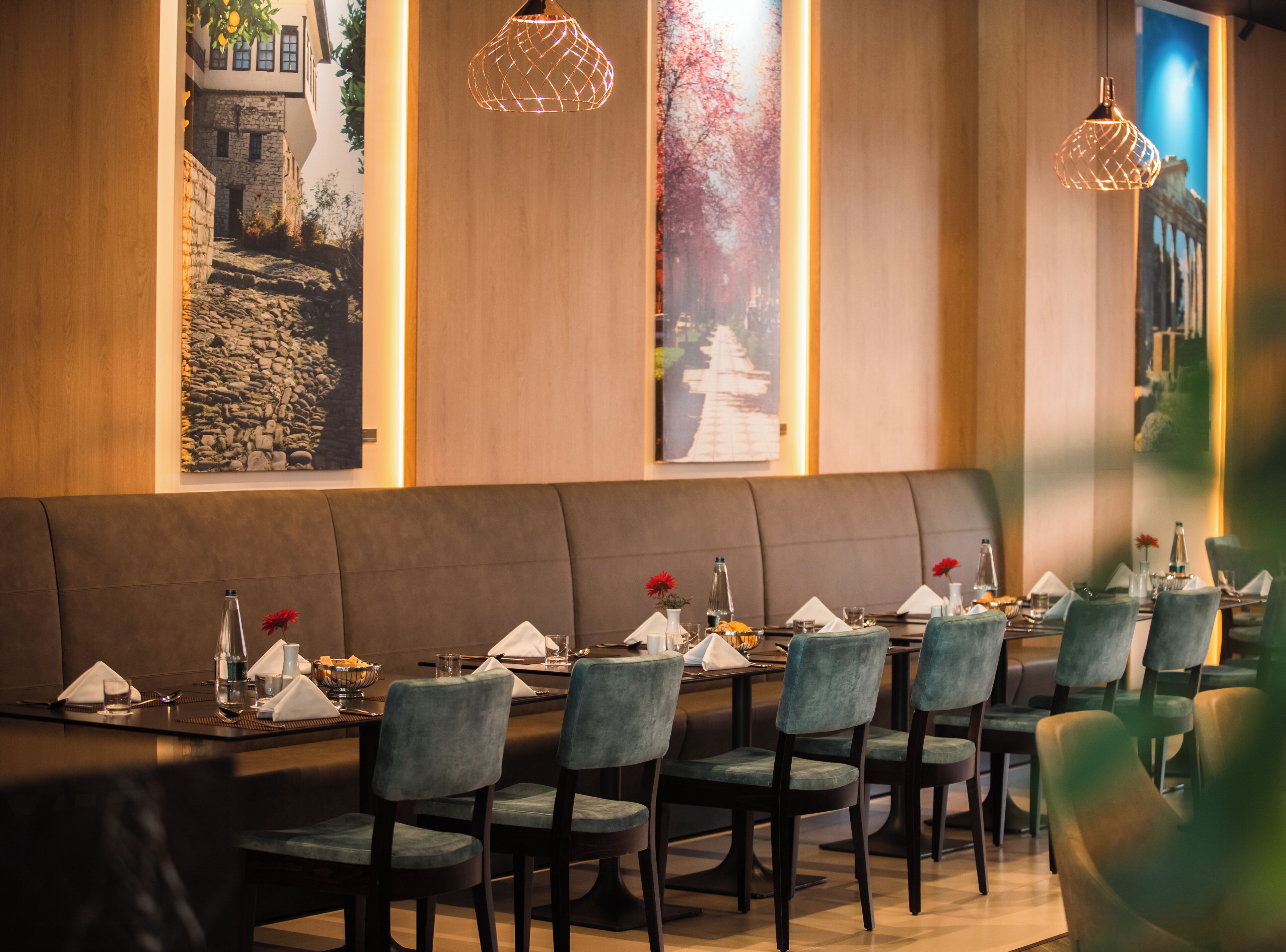 Un restaurante con una amplia zona de asientos tipo banco, varias mesas dispuestas para comer y lámparas colgantes.