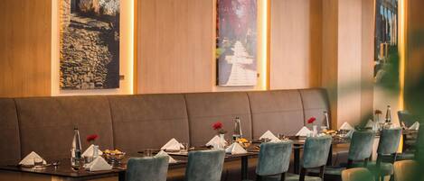 Un restaurante con una amplia zona de asientos tipo banco, varias mesas dispuestas para comer y lámparas colgantes.