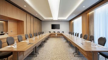 Un salón de conferencias con una mesa larga, sillas, un televisor de pantalla plana y suelo alfombrado.