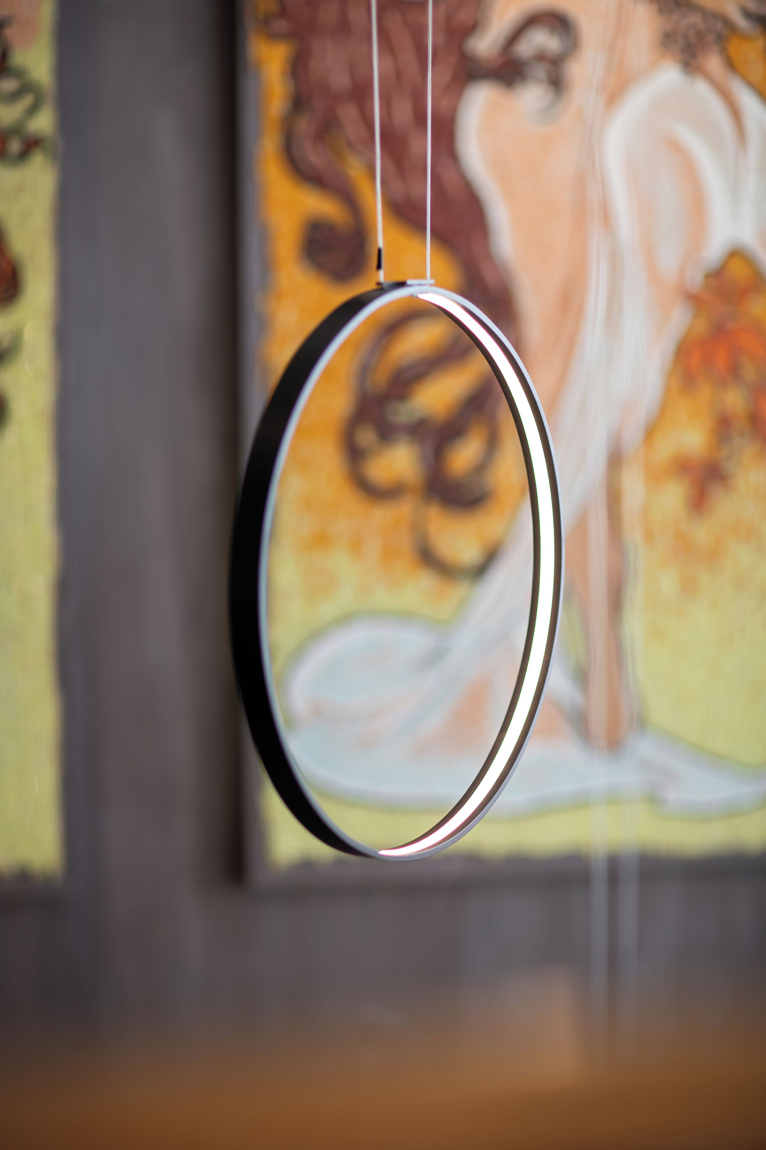 A circular object with a reflective surface, hanging against a wall with a blurred background featuring a painting.