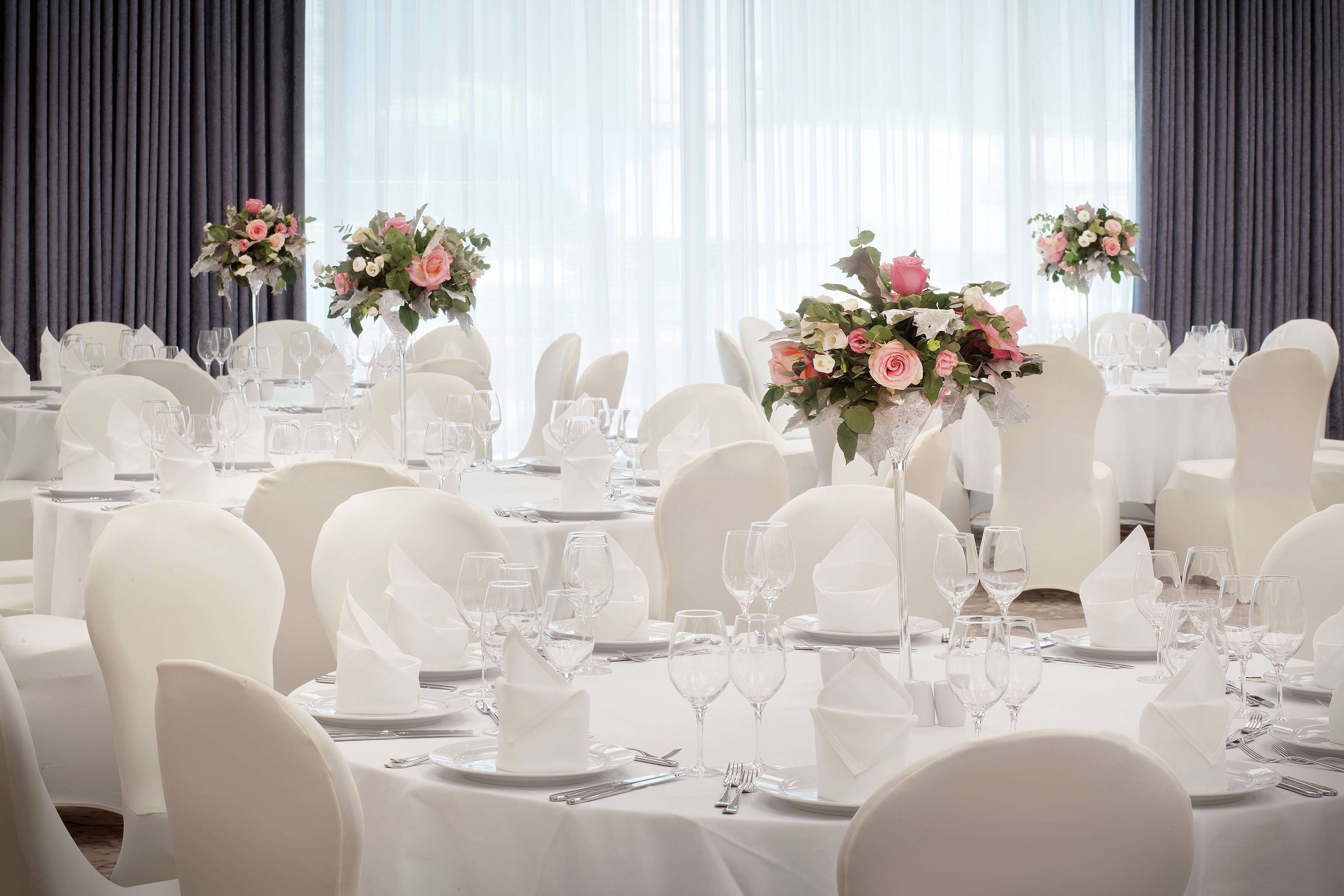 A banquet hall with round tables set for a formal event, complete with white tablecloths, glassware, and floral centerpieces.