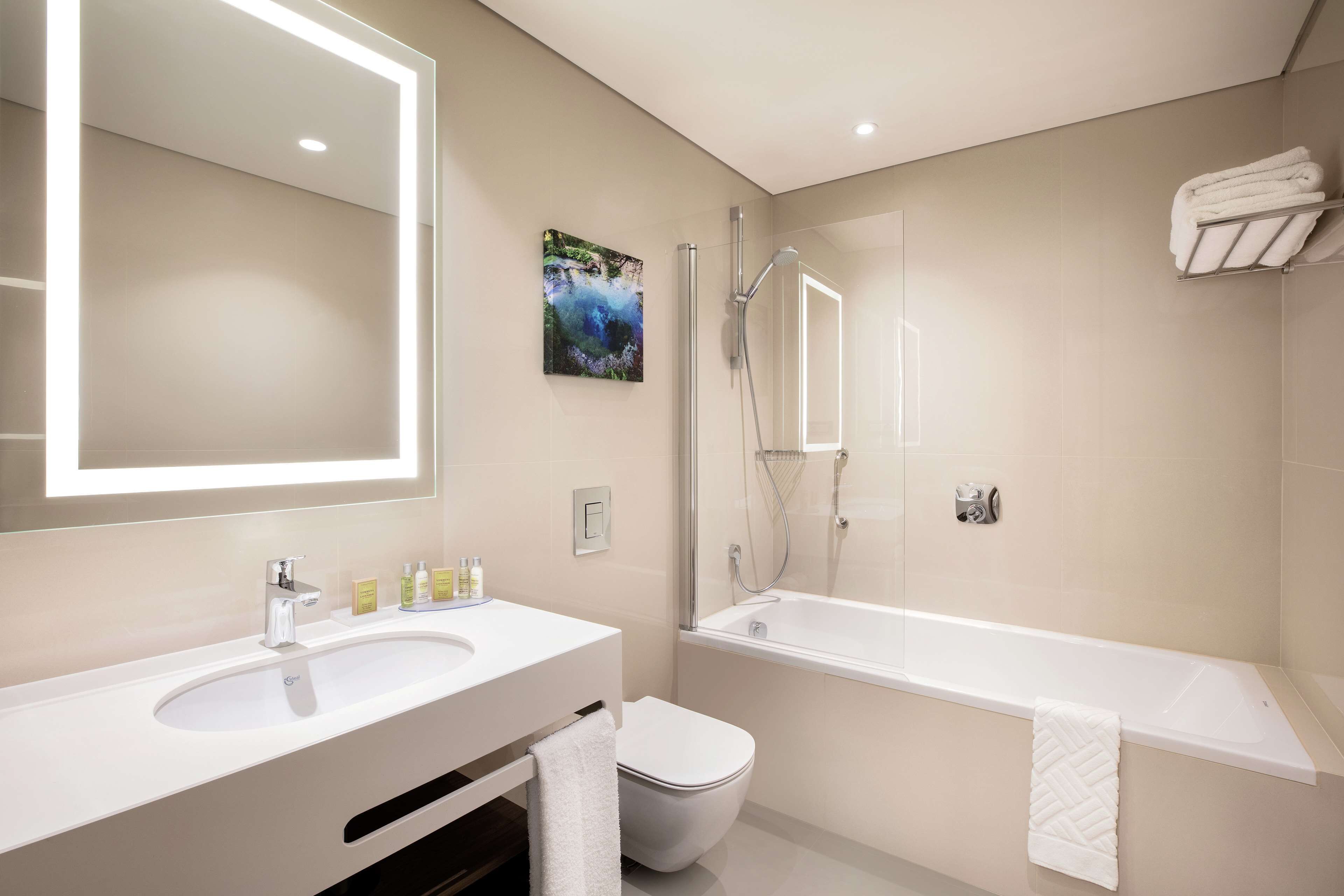A modern bathroom with a large mirror, a sink, a toilet, and a bathtub.