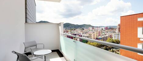 A balcony with two chairs and a small table, offering a view of a cityscape with buildings and hills in the background.