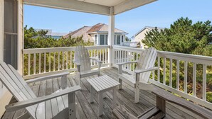 Eine überdachte Veranda mit weißen Holzstühlen und einem Tisch, mit Blick auf eine Wohngegend mit Häusern und Bäumen.