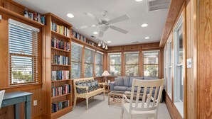 Ein gemütlicher Lesesaal mit Holzbücherregalen, einem Schaukelstuhl, einer Couch und einem Tisch.