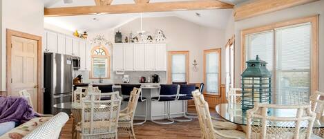 A spacious kitchen with white cabinets, a stainless steel refrigerator, and a dining area with wicker chairs and a glass table.