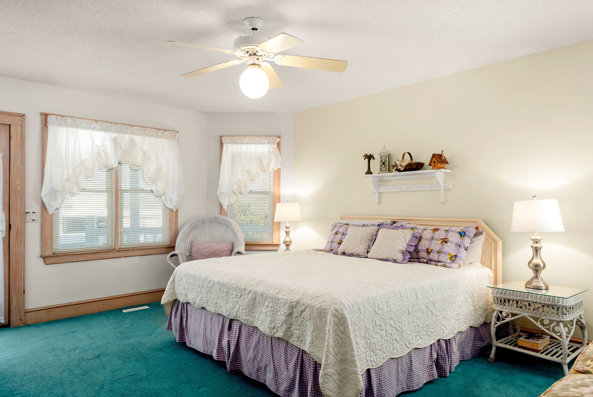 A bedroom with a bed, a chair, a ceiling fan, and a nightstand with a lamp.