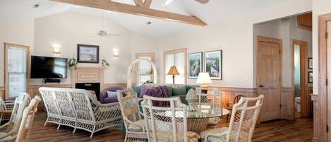 A spacious living room with wicker furniture, a fireplace, and a ceiling fan.