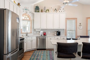 A modern kitchen with white cabinets, stainless steel appliances, and a dining area with dark chairs.