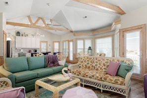 A spacious living room with a green sofa, a patterned sofa, and a wicker coffee table. There is a swan decoration on the table.
