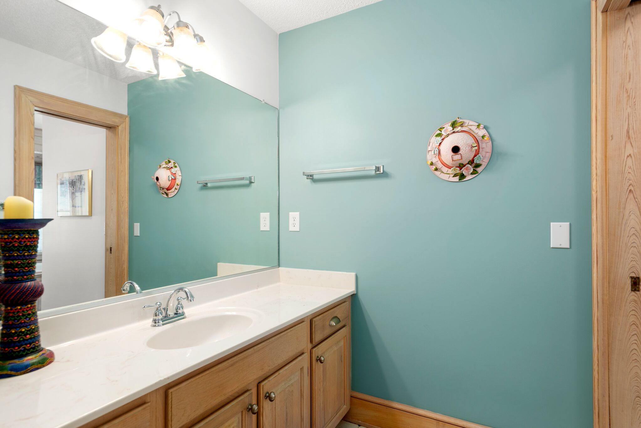 A bathroom with a large mirror, a sink, wooden cabinets, and a teal wall.
