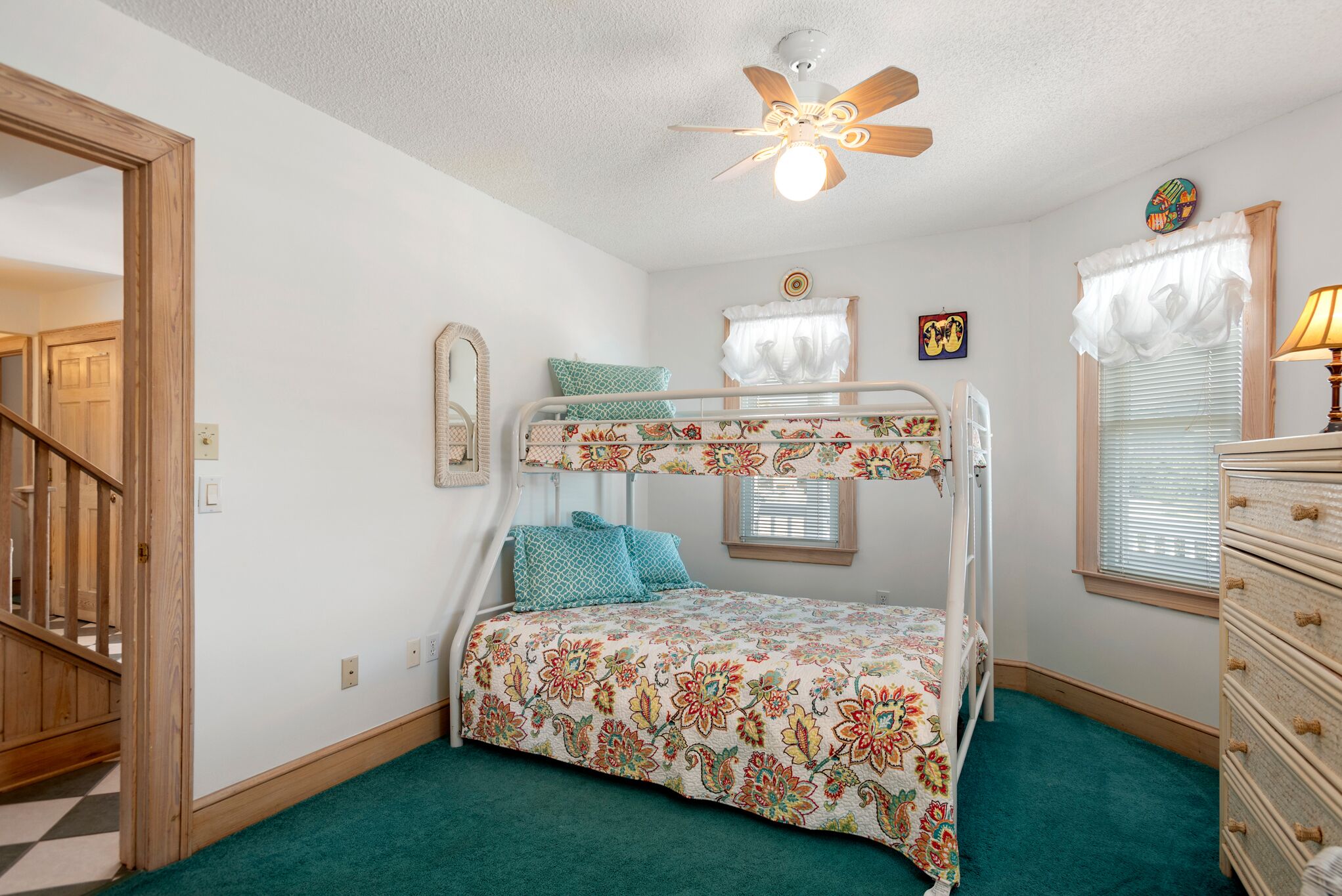 A bunk bed with floral bedding, a ceiling fan, a dresser, and a window with blinds.