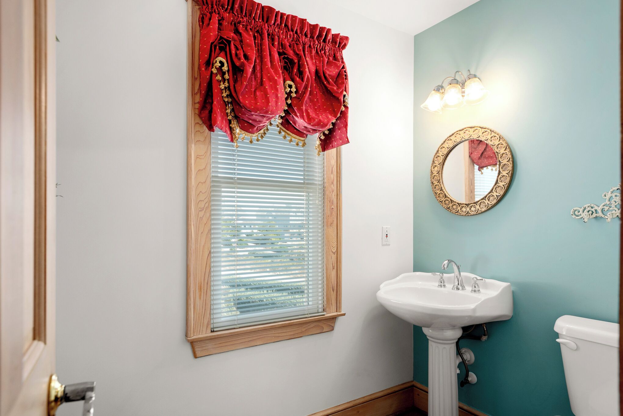A bathroom with a window, a sink, a toilet, and a mirror with a decorative frame.