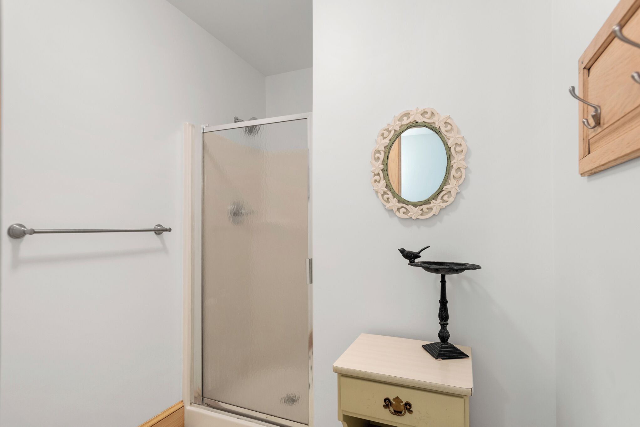 A bathroom with a glass shower door, a towel rack, a vanity with a mirror, and a bird sculpture.