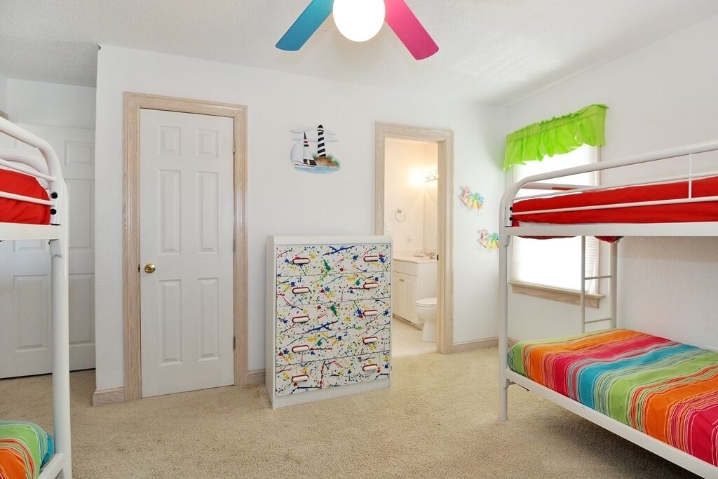 A bunk bed room with a colorful striped bedspread, a white door, and a small shelf with a nautical-themed decoration.