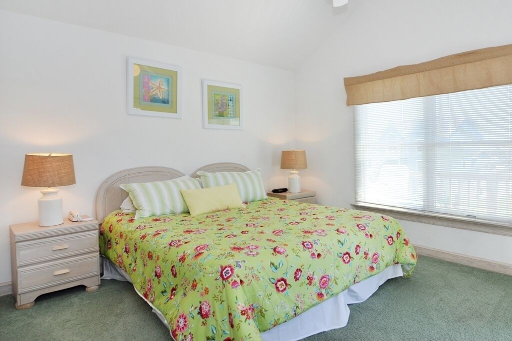 A bedroom with a floral bedspread, two bedside lamps, a nightstand, and a window with blinds.