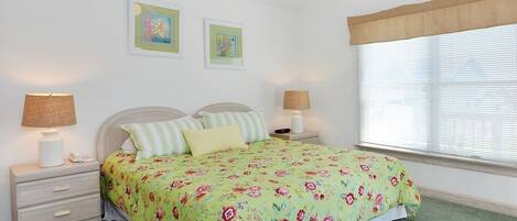 A bedroom with a floral bedspread, two bedside lamps, a nightstand, and a window with blinds.