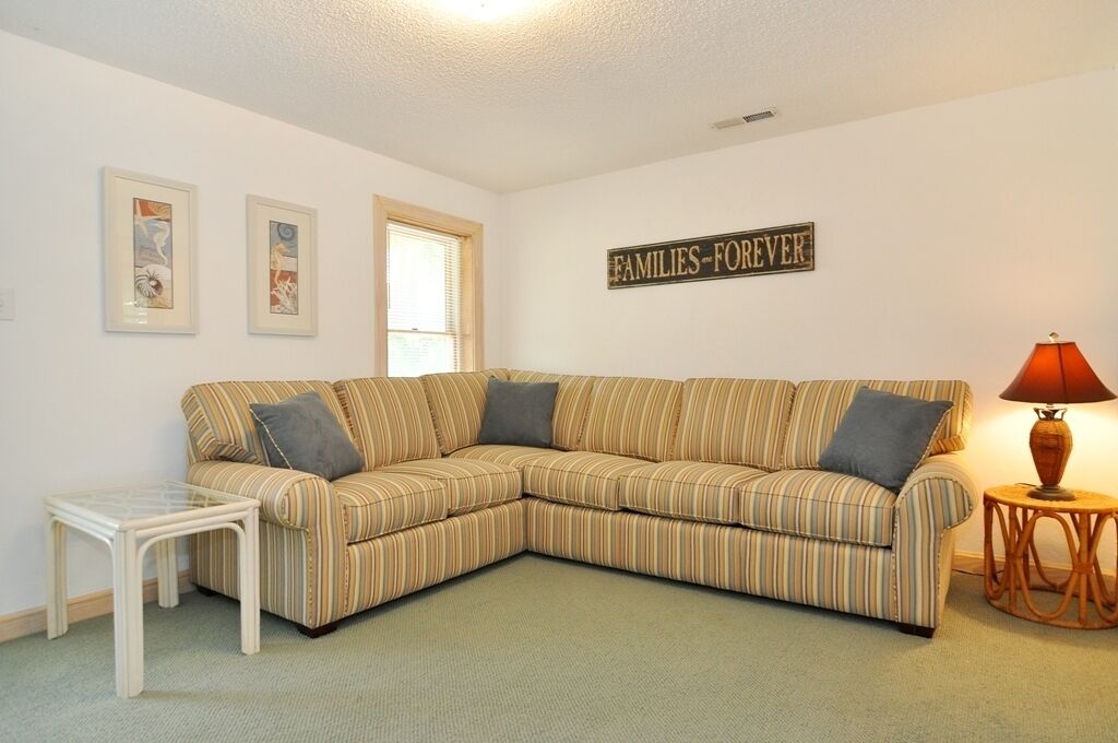 A living room with a striped sectional sofa, a small white table, a lamp, and framed artwork on the wall.