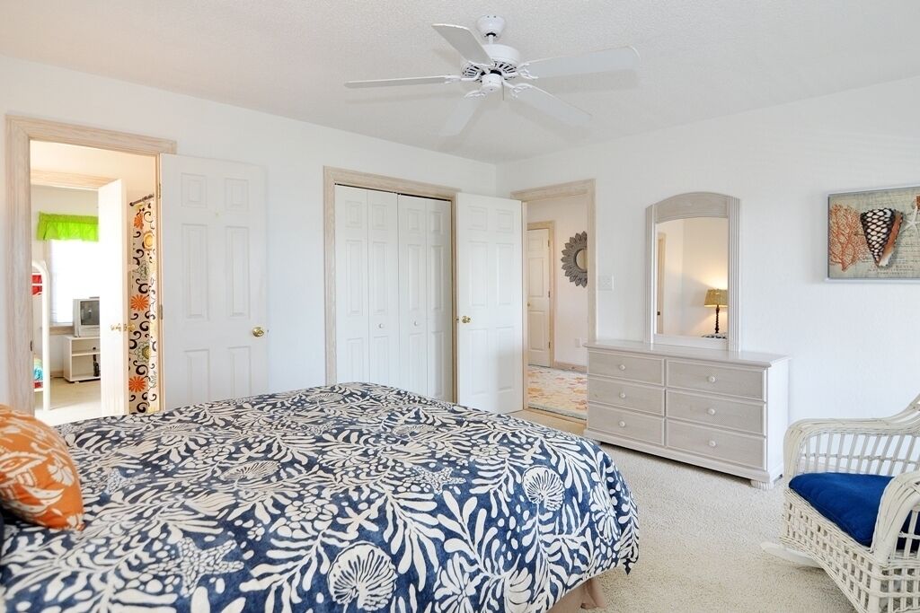 Une chambre à coucher comprenant un lit, une commode, une chaise et un ventilateur de plafond.