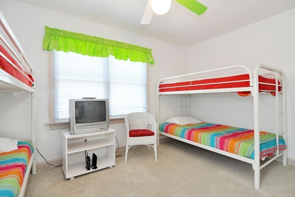 Une chambre d’enfant avec des lits superposés, un téléviseur posé sur un meuble et une fenêtre avec des stores.