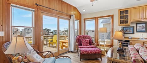 A spacious living area with wooden walls, large windows, a ceiling fan, and a balcony with outdoor furniture.