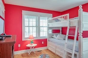 A room with a bunk bed, a desk, a lamp, and a window.