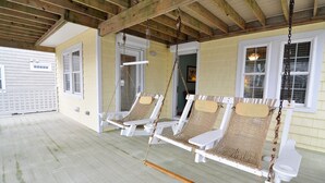 A porch with two white wicker swing chairs and a small table. - Heels In The Sand: Close to beach, Private Pool (Nags Head)