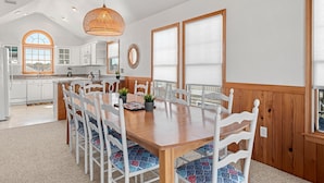 A spacious kitchen with white cabinets, a wooden dining table, and a large window.