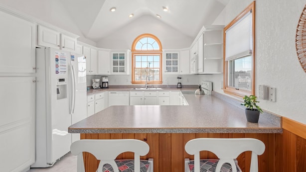 A kitchen with white cabinets, a granite countertop, and a large window with a wooden frame.